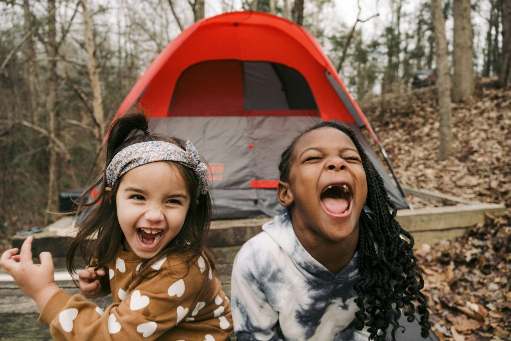Deux enfants rient devant une tente de camping en forêt