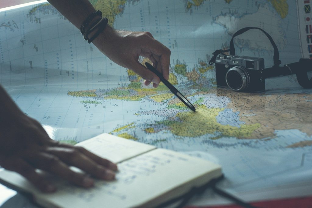 Main qui pointe un itinéraire sur une carte avec carnet et appareil photo