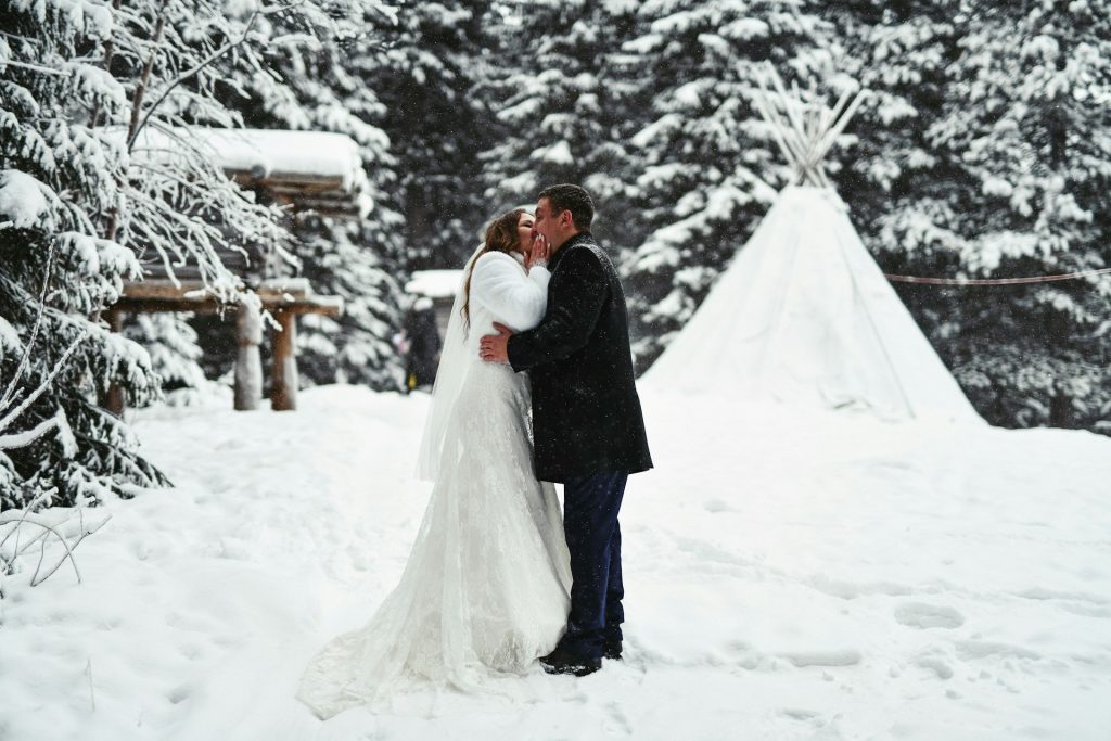 Mariés qui s’embrassent dans la neige devant un tipi