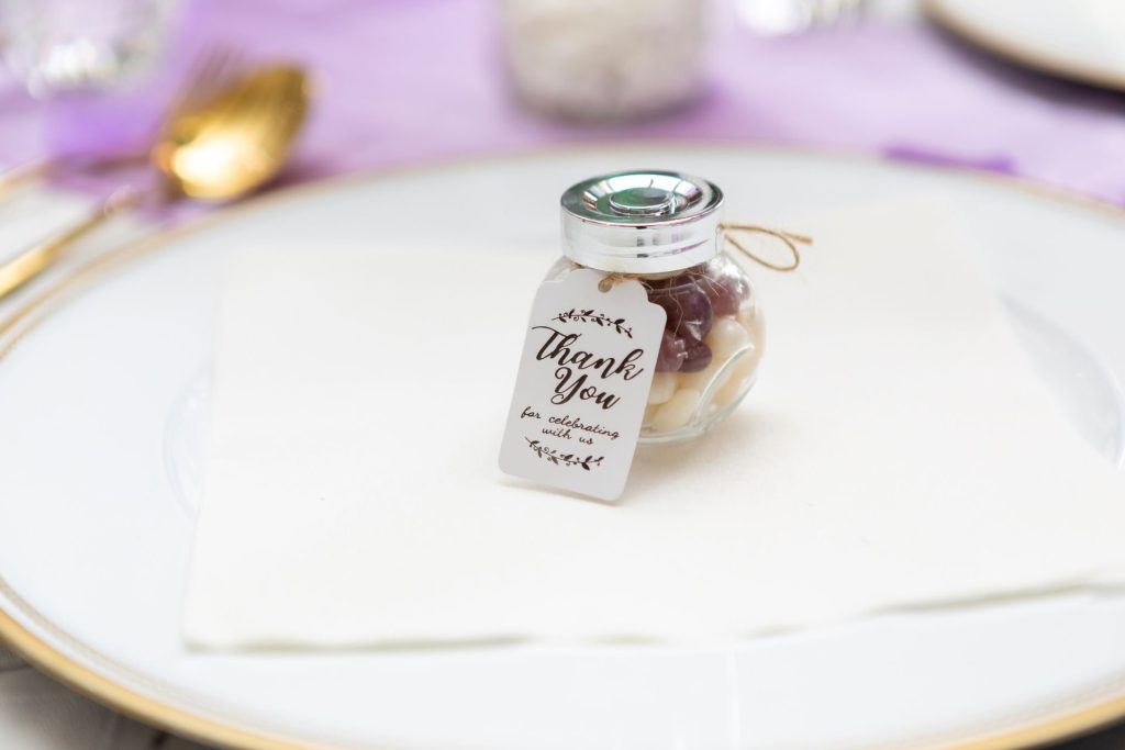 Petit pot cadeau avec étiquette de remerciement posé sur une assiette de mariage