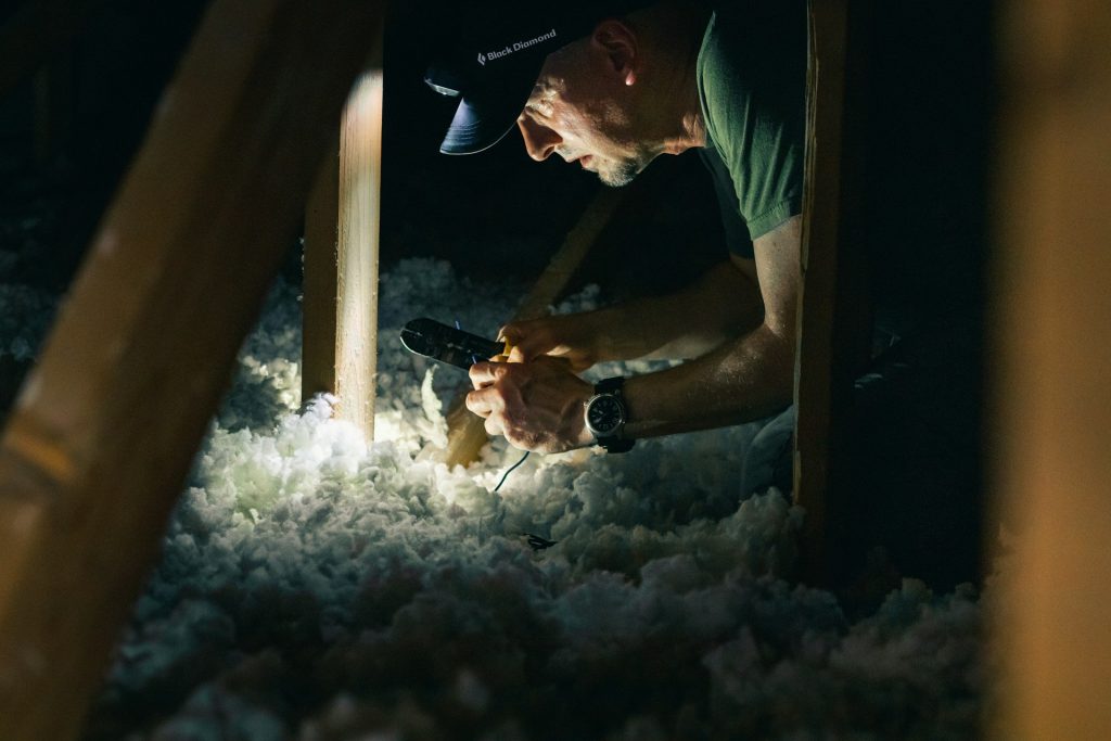 Un homme éclairé par une lampe inspecte l’isolant dans des combles